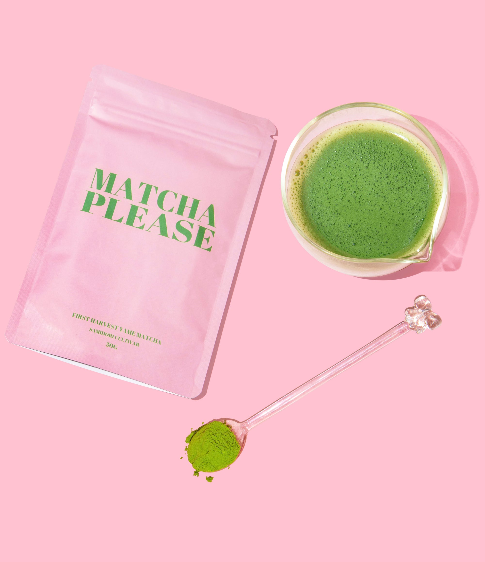 Matcha green tea powder package with a glass of matcha and a spoon on a pink background